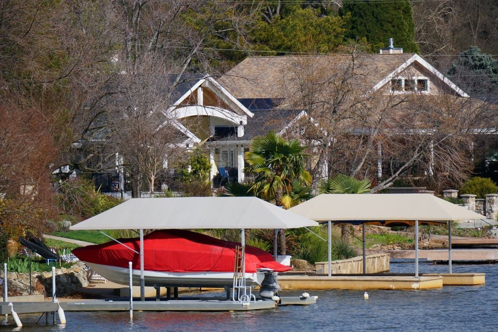 Red boat under a covered dock on a lakeside with houses in the background
