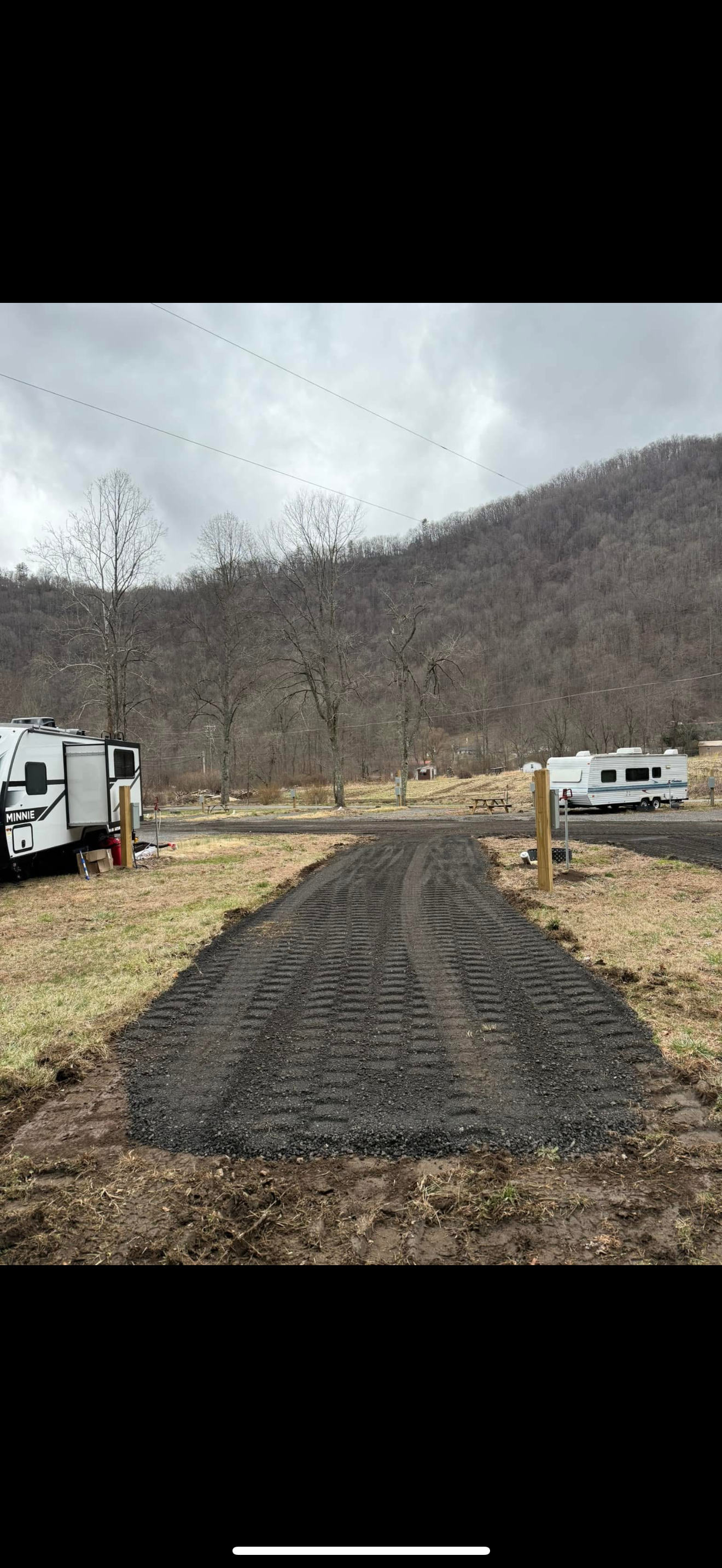 A gravel road leads to campsites with RVs, set against a mountain backdrop under a cloudy sky.