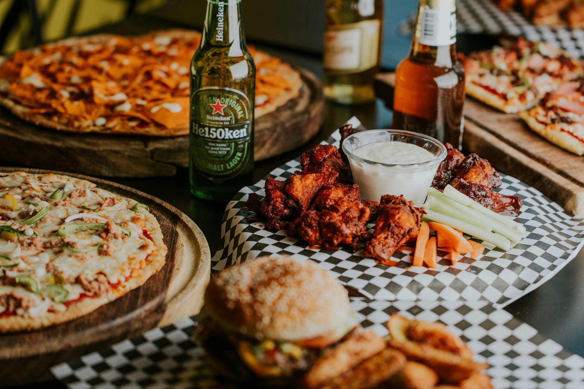 Pizza, chicken wings, burger, and beer on a table; food spread.