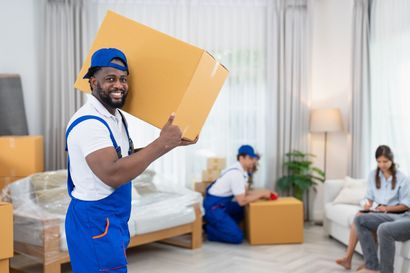 A man is carrying a cardboard box in a living room.