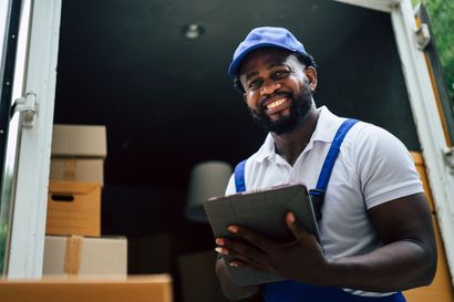 A delivery man is holding a tablet in front of a truck.