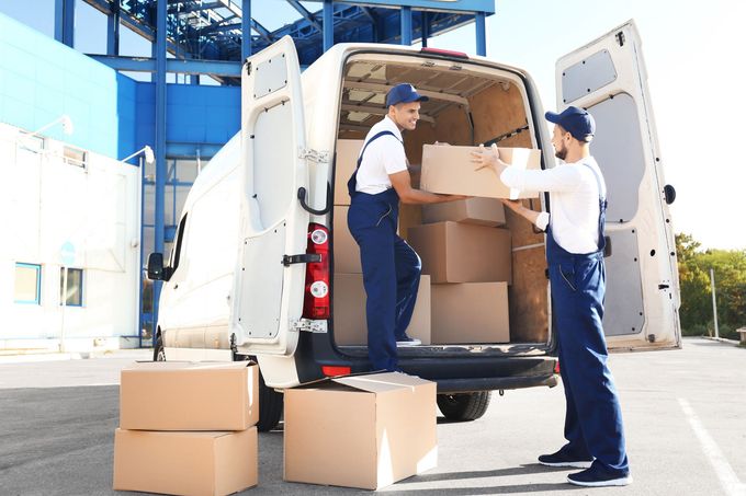 Two delivery men are loading boxes into a van.