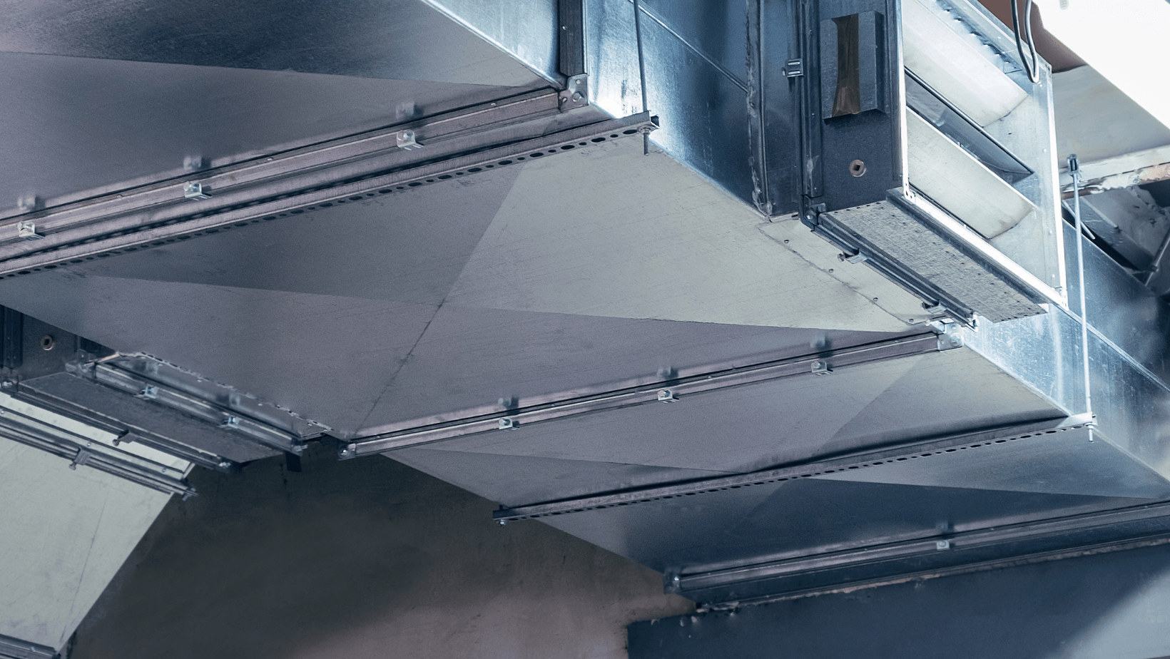 Metal HVAC ductwork and ventilation system inside an industrial ceiling area.