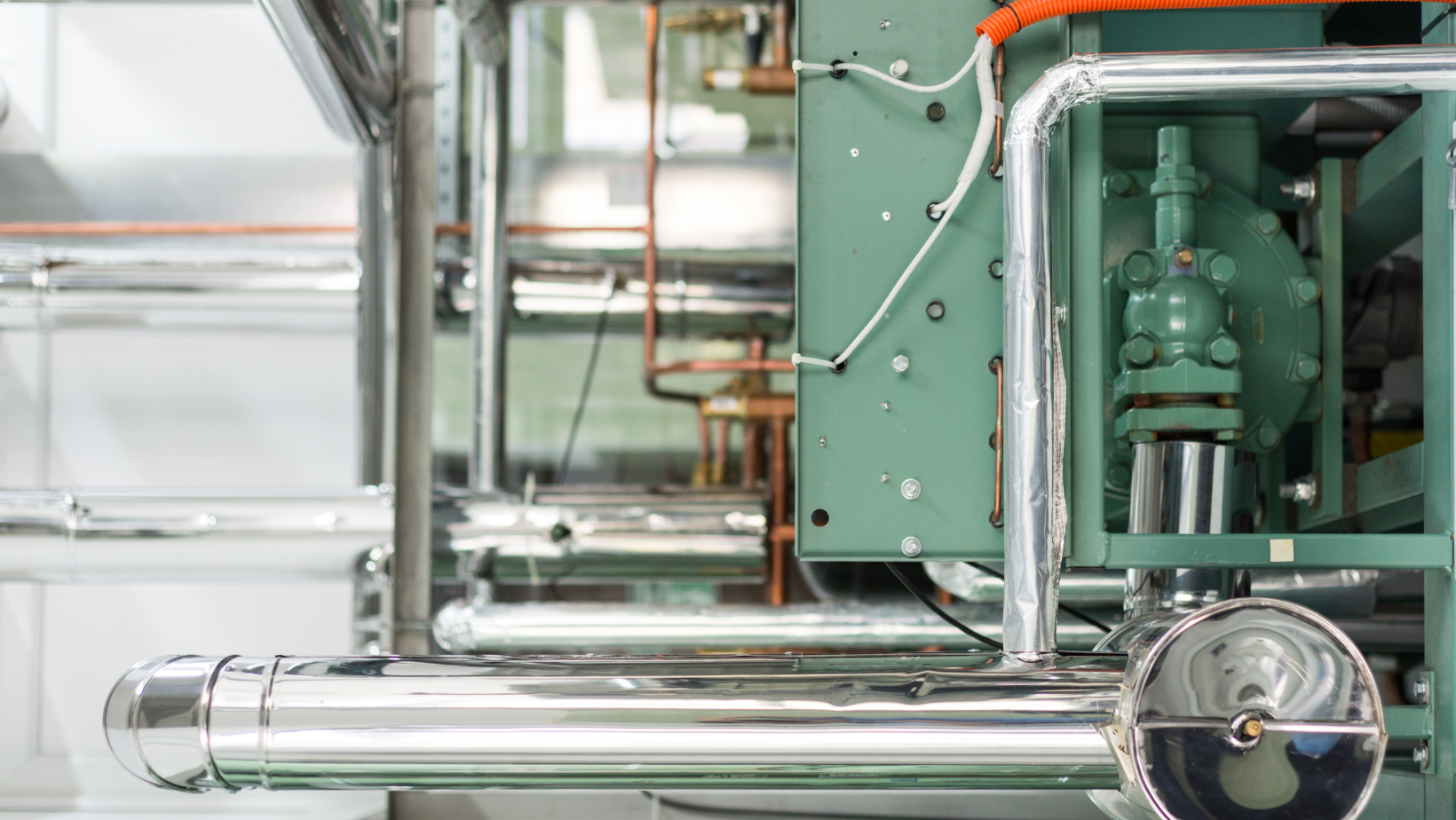 Industrial pipes and machinery with shiny metal tubing and green equipment in a factory setting