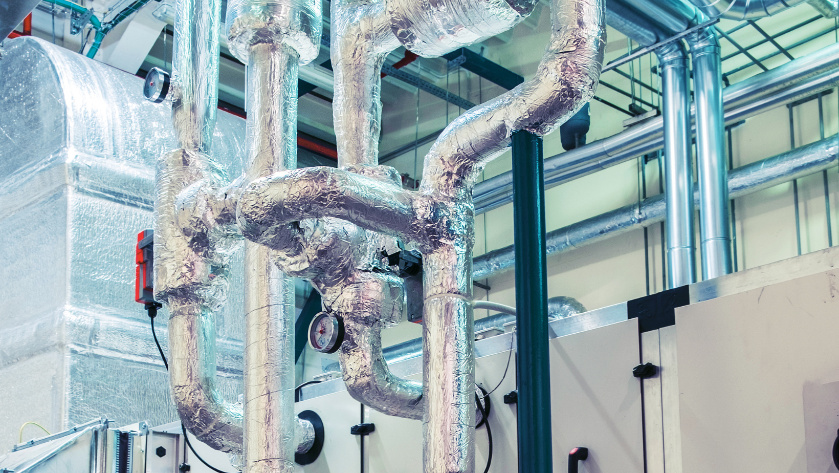 Insulated industrial pipes and ducts in a mechanical room with silver foil wrapping and blue supports