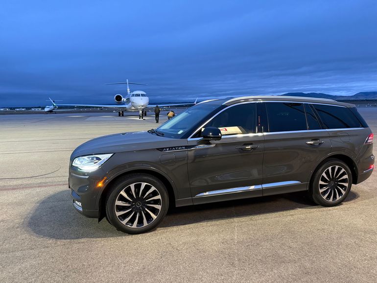 Dark SUV parked on a runway with a private jet in the background at dusk.