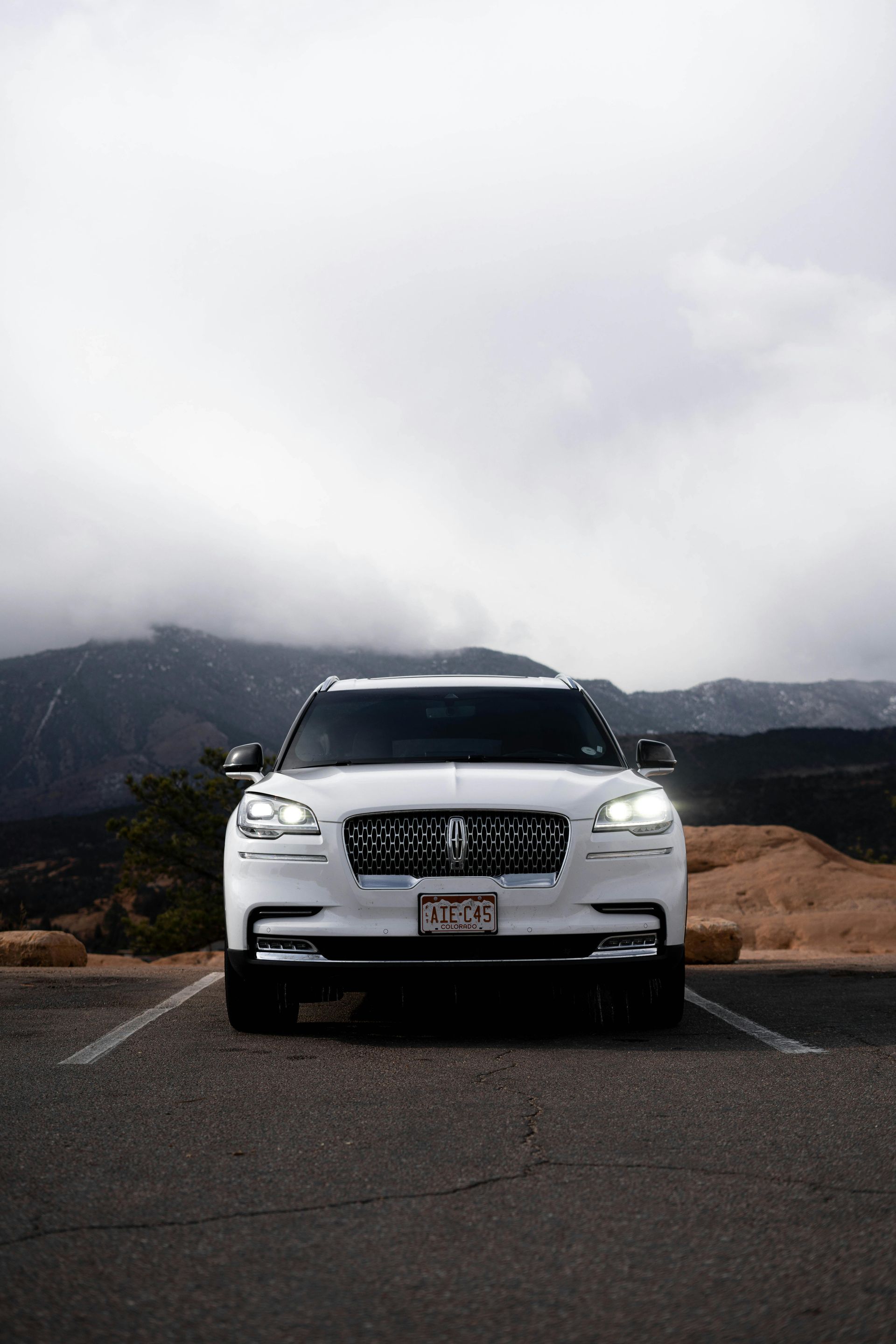 White car parked on a road with mountains and cloudy sky in the background