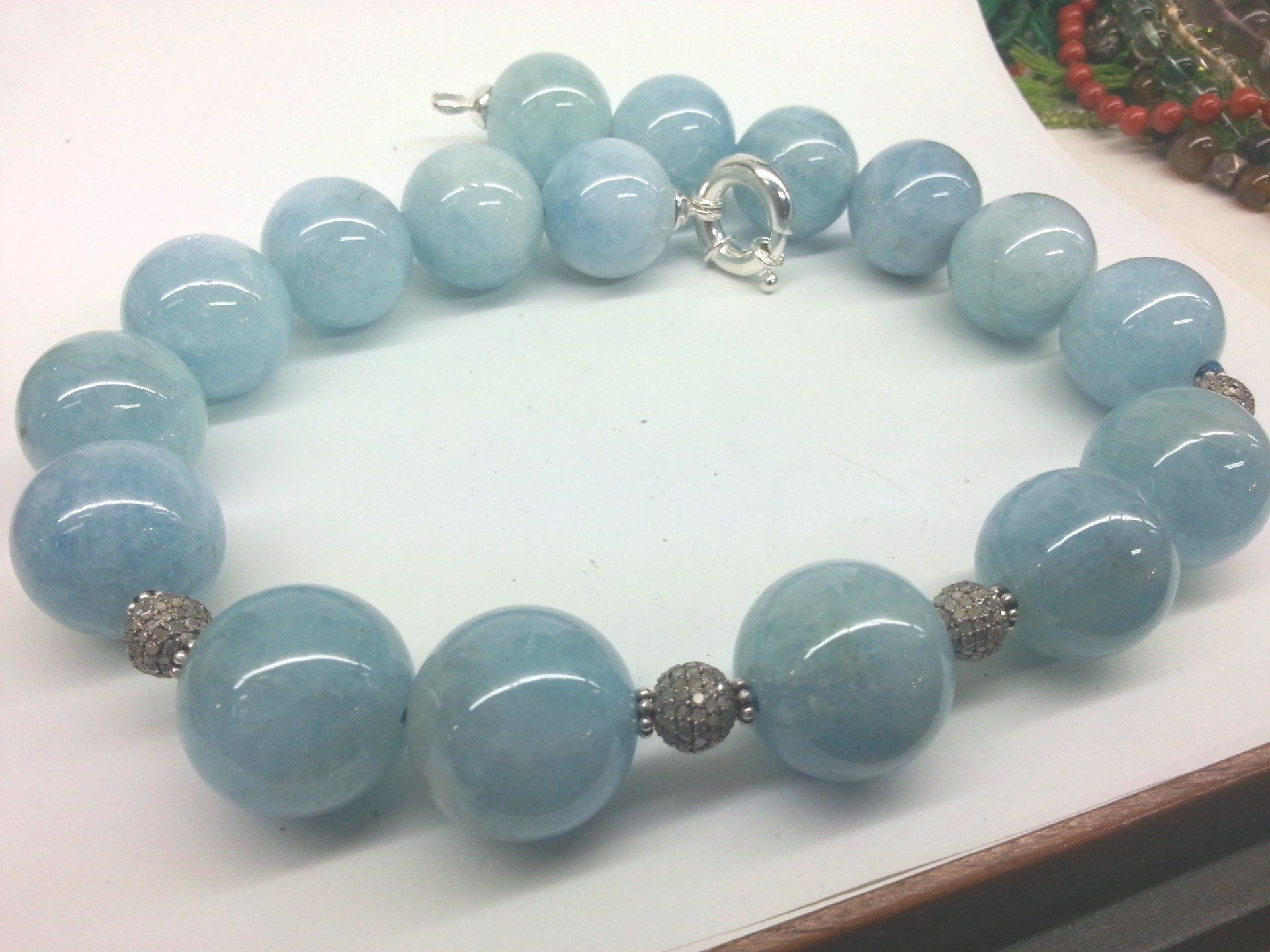 Collana di perline di pietre preziose azzurre con distanziatori sferici in argento e chiusura a moschettone su sfondo bianco.