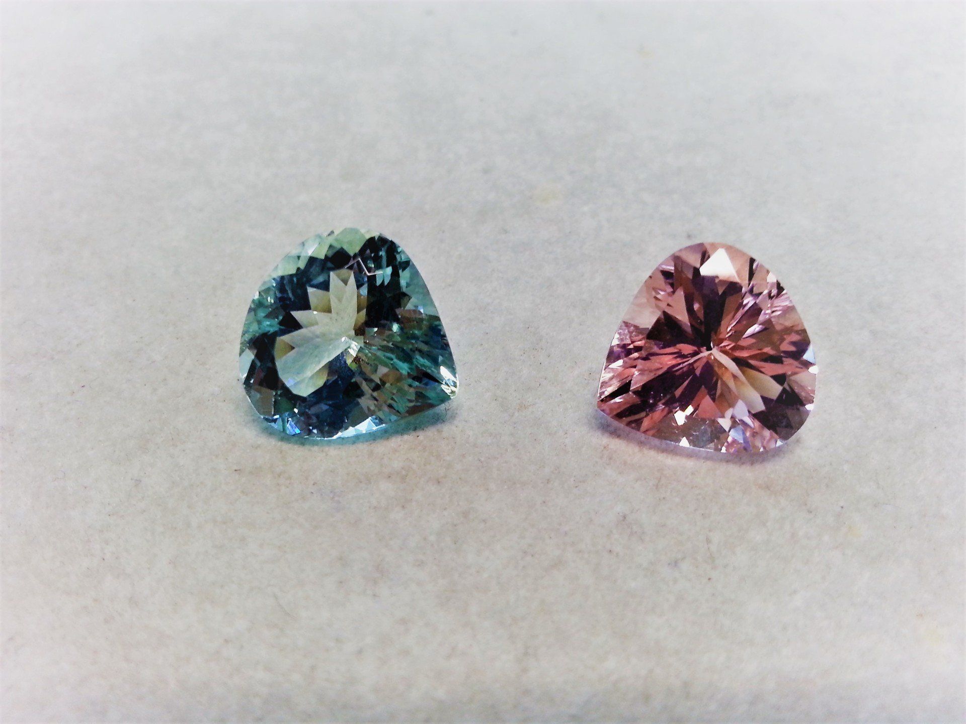 Due gemme sfaccettate a taglio triangolare poggiate su una superficie chiara: una è di colore blu turchese e l'altra di rosa chiaro.