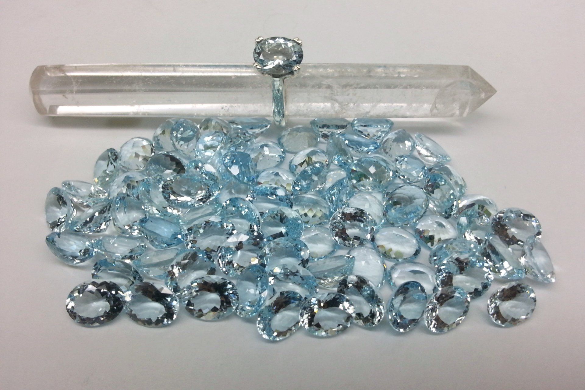 Un anello con una gemma blu sfaccettata poggia su un quarzo cristallino trasparente, a sua volta adagiato su un mucchio di pietre blu ovali sciolte.