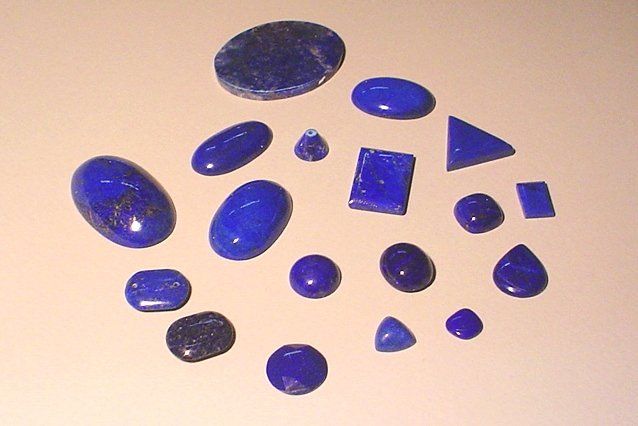 Una collezione di gemme di lapislazzuli lisce e levigate, di varie forme e dimensioni, disposte su uno sfondo chiaro.