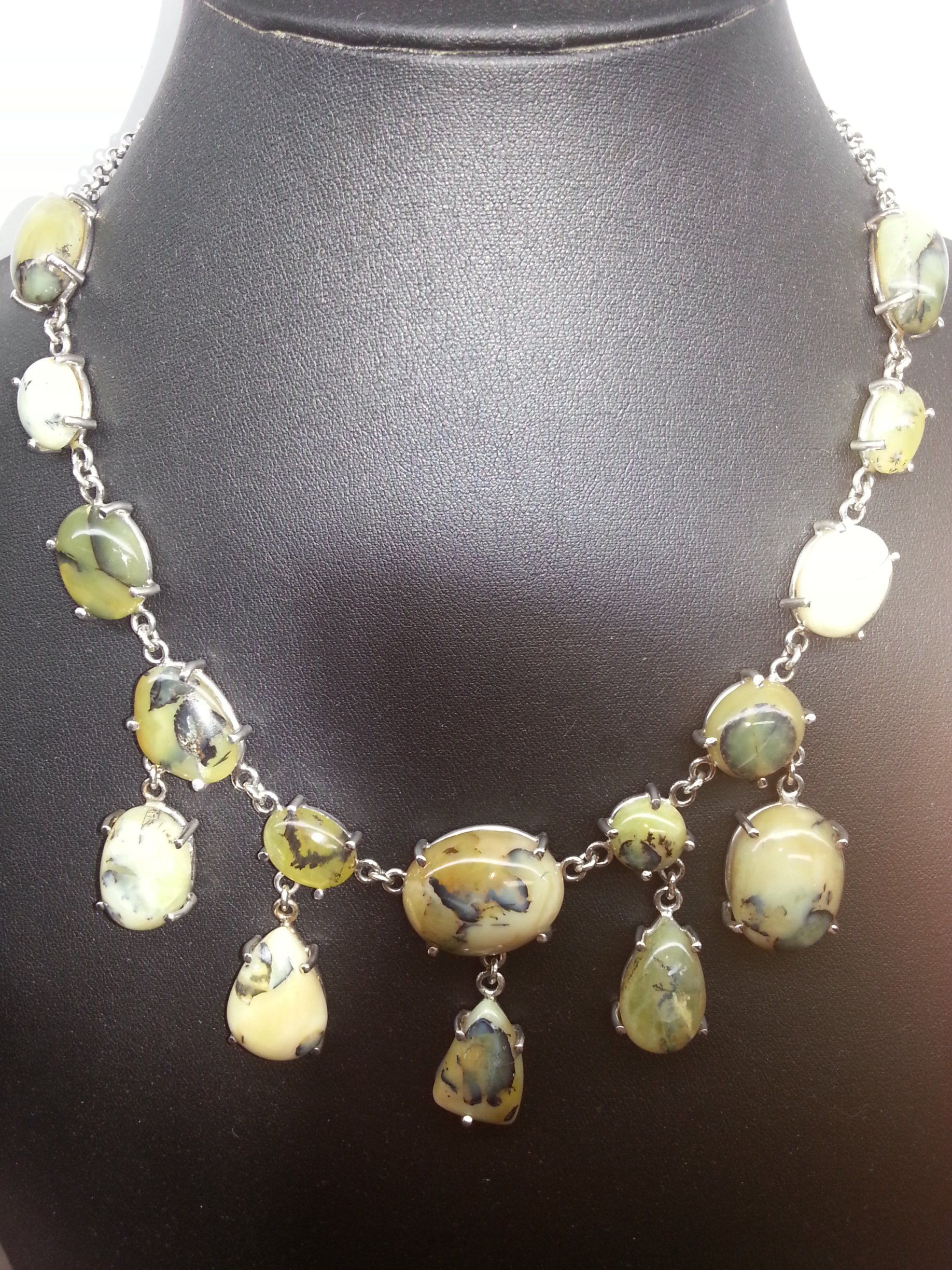 Una collana con pietre screziate di giallo e verde di varie forme, incastonate in metallo argentato su una base scura.