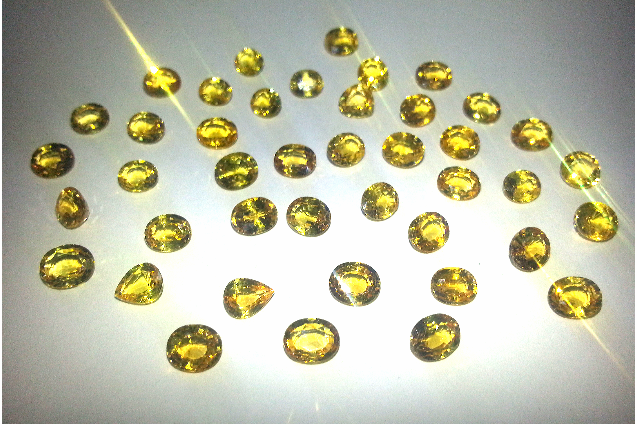 Una collezione di piccole gemme sfaccettate color oro giallo, sparse su uno sfondo chiaro e neutro.