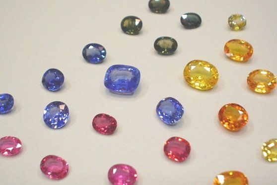 Una collezione di gemme sfaccettate di vari colori, tra cui diverse tonalità di blu, giallo, rosso e grigio scuro, su sfondo bianco.