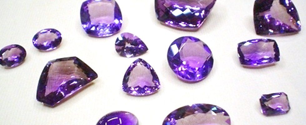 Una distesa di ametiste viola levigate, di varie forme e dimensioni, su uno sfondo bianco.
