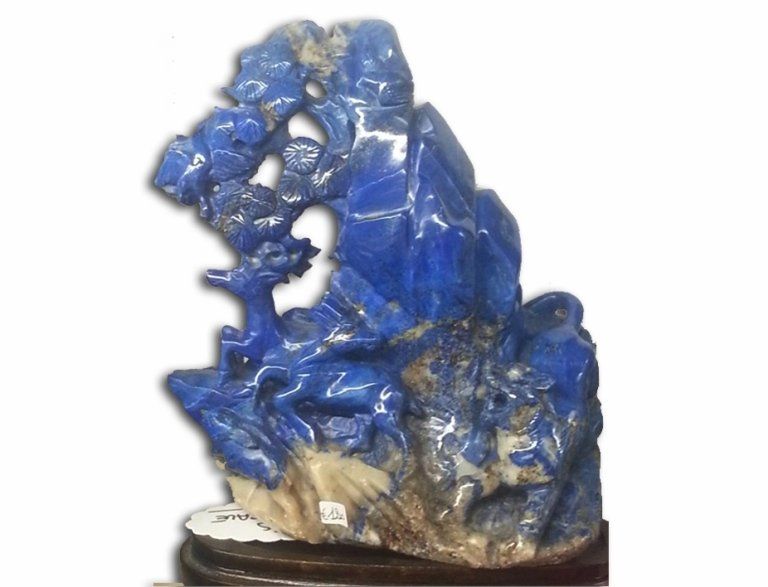 Una scultura in lapislazzuli di un blu intenso, raffigurante un paesaggio montano con cervi, posta su una base di legno scuro.
