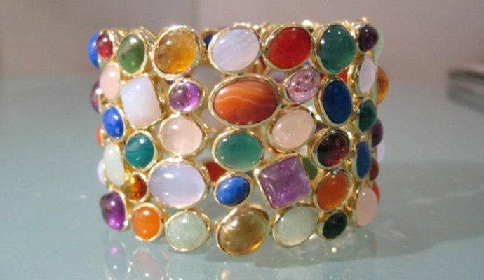 Un ampio bracciale rigido in oro con un assortimento di pietre semipreziose colorate, lucide, di forma ovale e quadrata.