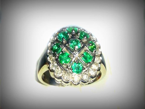 Anello in oro con un gruppo di smeraldi rotondi circondati da un alone di piccoli diamanti in una montatura color argento.
