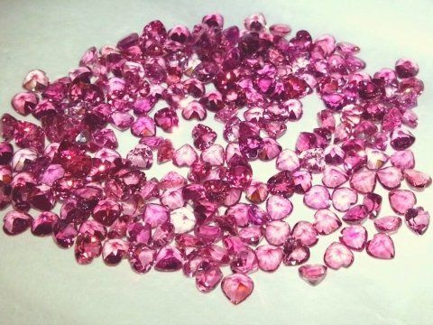 Un grande mucchio di gemme rosa sfaccettate a forma di cuore, sparse su uno sfondo bianco.