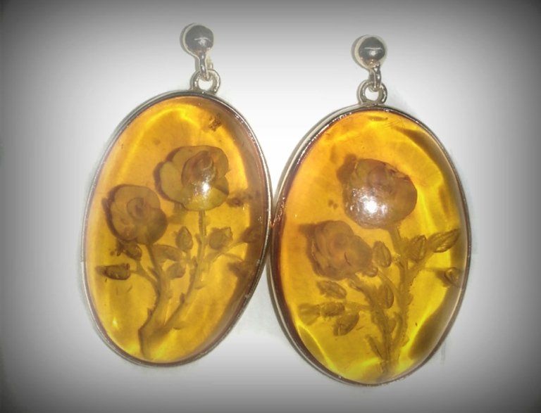 Un paio di orecchini ovali in ambra giallo-dorata, ciascuno caratterizzato da un'elaborata incisione a rilievo di una rosa con foglie.