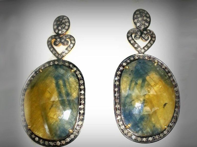 Un paio di orecchini pendenti ovali caratterizzati da grandi pietre sfaccettate di colore giallo e blu, incorniciate da minuscoli diamanti.