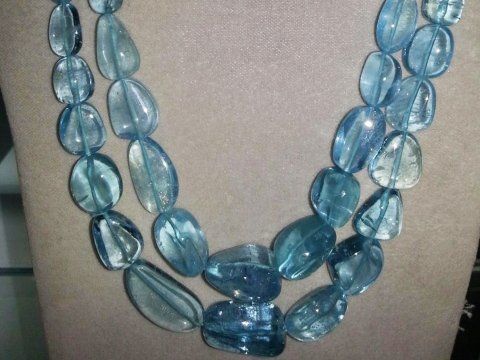 Una collana a più fili composta da perle di pietra azzurra traslucida e lucida, disposte in un disegno ovale e a scalare.