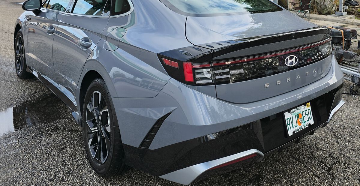 Gray sedan parked on a wet lot, rear three-quarter view with black wheels and taillights lit