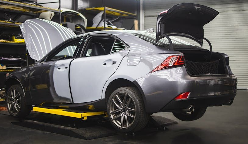 Silver sedan with open hood, trunk, and doors on a yellow car lift in a garage