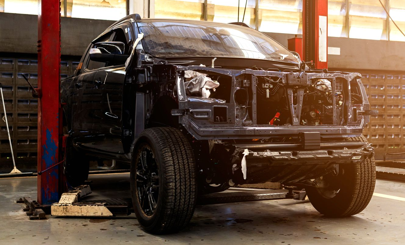 Damaged black pickup truck in an auto repair shop, front end exposed on a lift