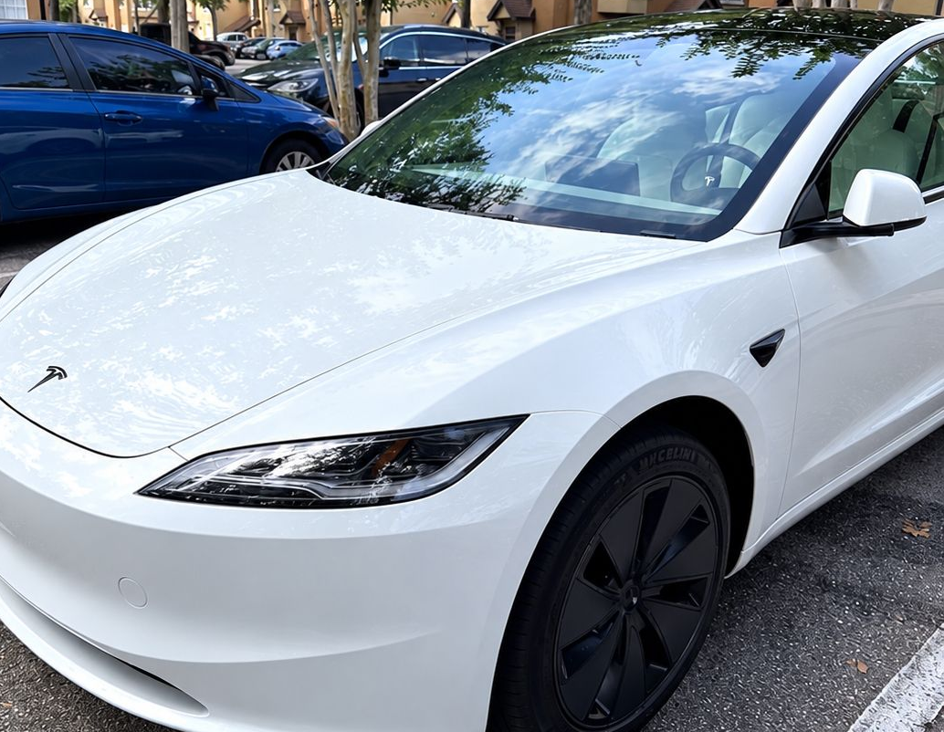 White Tesla sedan parked on a tree-lined street, front three-quarter view