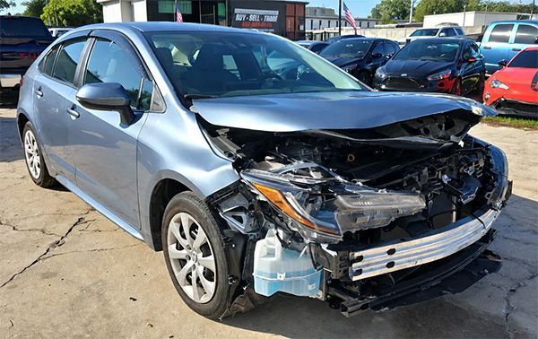 Damaged black SUV in an auto shop, front end removed and hood crumpled, lifted on a rack.