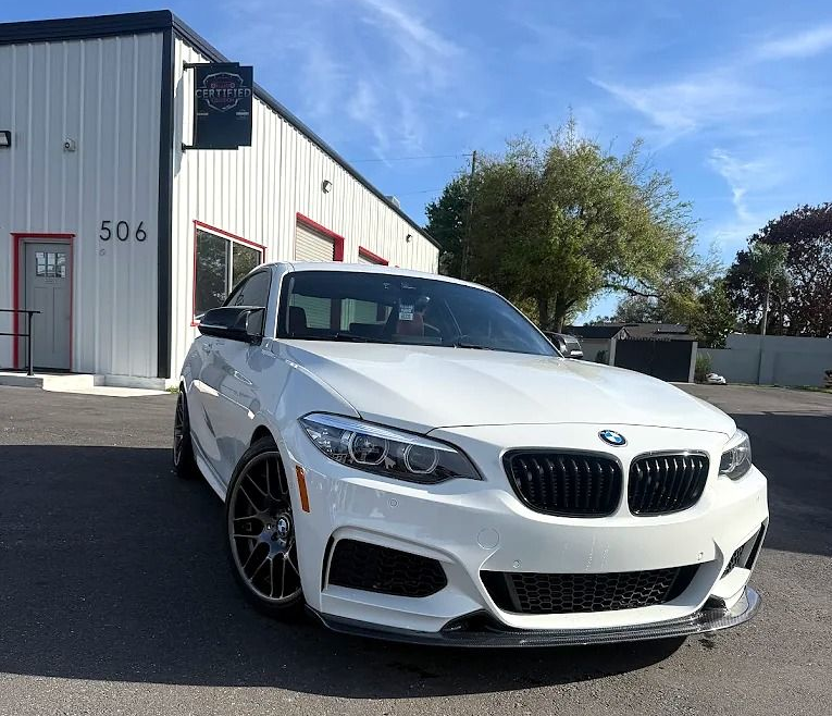 White BMW coupe parked outside a gray industrial building on a sunny day