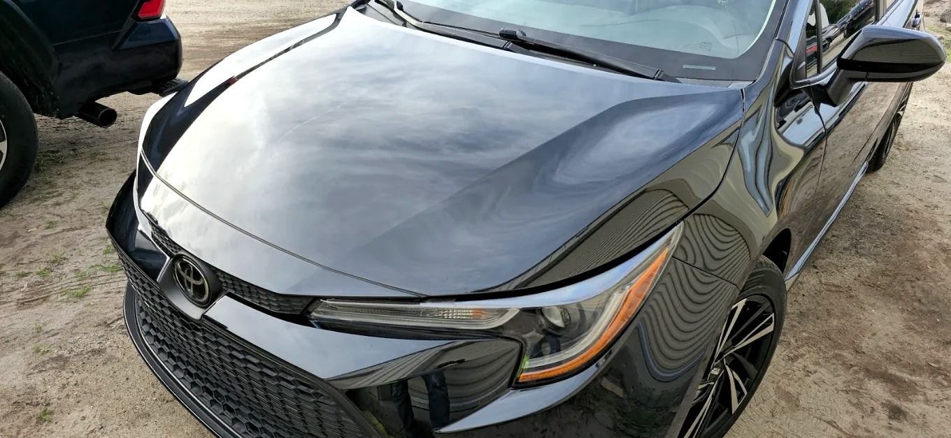 Black sedan parked on a gravel lot, front view with a damaged grille and hood