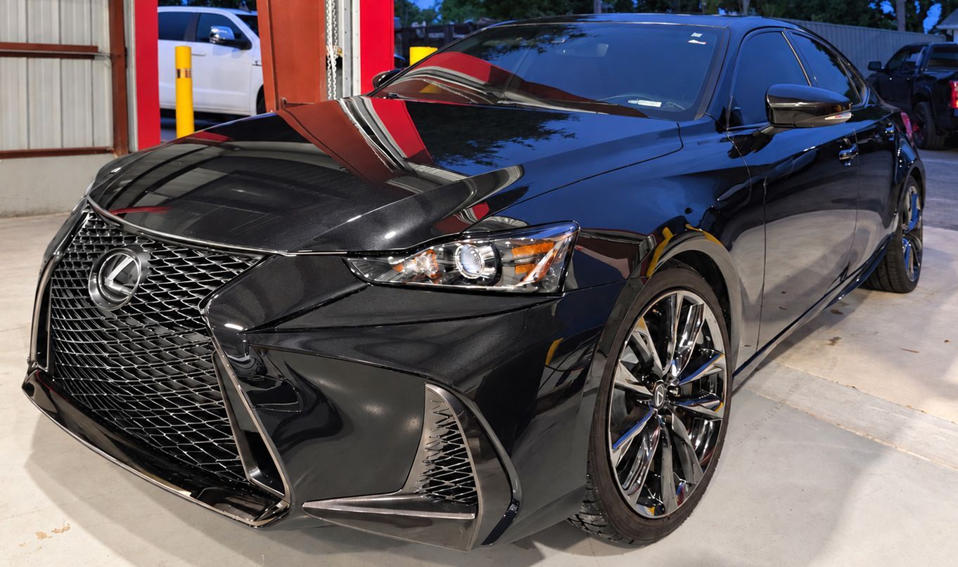 Black Lexus sedan parked indoors under bright lights, front-left view, with a red door open nearby