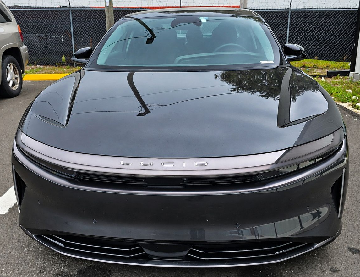 Front view of a dark gray car parked in a lot, with a chain-link fence in the background.