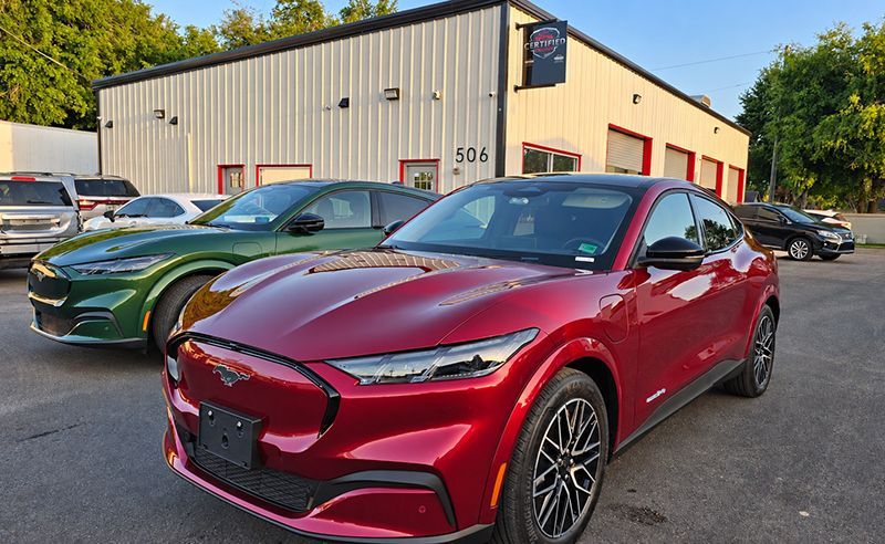 Red Mazda SUV parked in front of a beige industrial building, with a green sports car behind it.