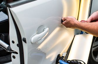 Person removing a white car door panel with a tool during vehicle repair