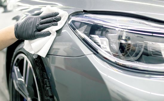 Hand polishing a black car’s front fender with a yellow orbital buffer