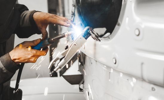 Mechanic welding a white car body, bright blue sparks flying in the garage