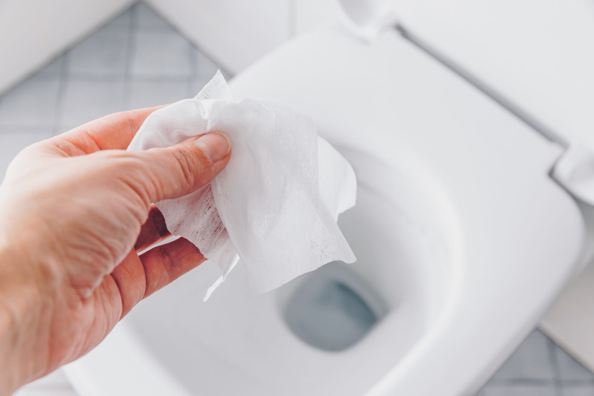 Hand wiping a white toilet seat with a tissue or wipe