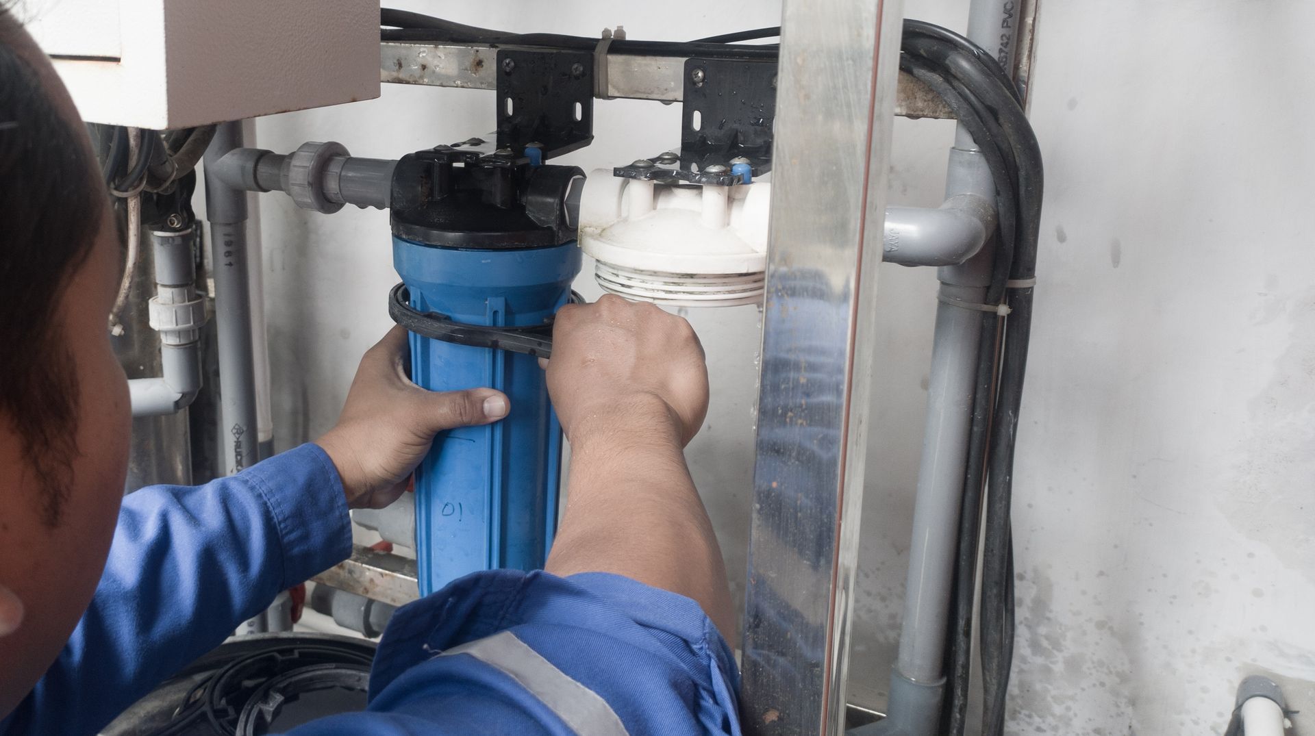 A technician in blue coveralls servicing a blue water filter housing.