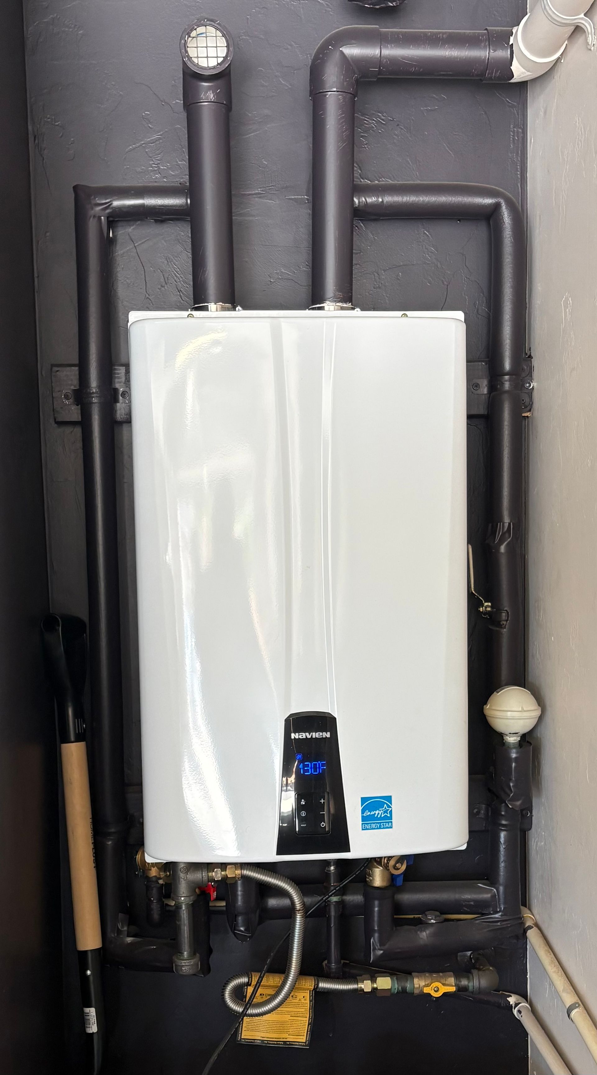 White wall-mounted boiler with black pipes and yellow gas lines in a utility room