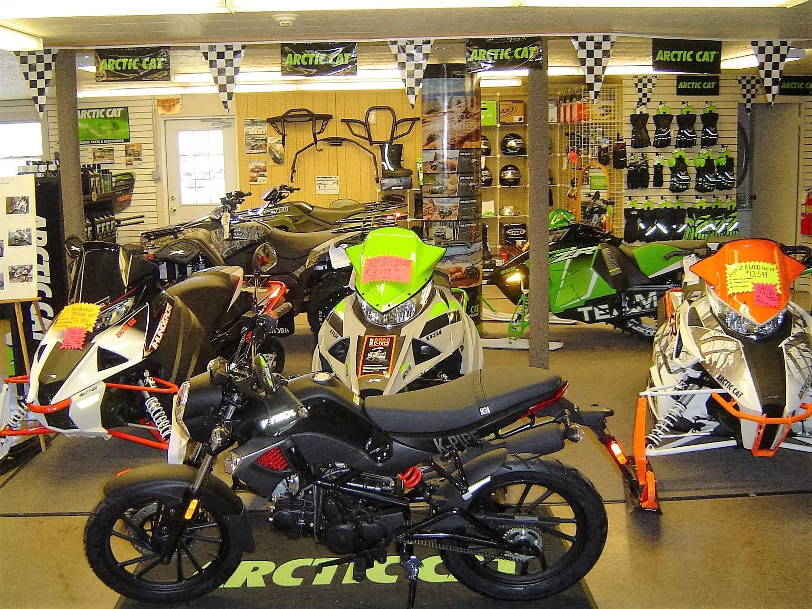 Motorcycle in a showroom, surrounded by snowmobiles, helmets, and accessories. Arctic Cat branding.