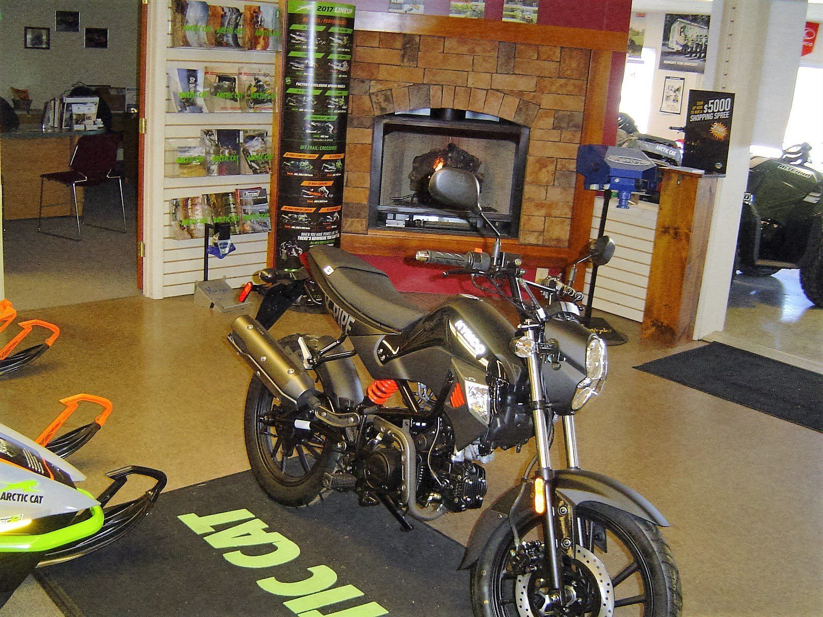 Black motorcycle in a showroom, with fireplace in background. Arctic Cat mat in foreground.