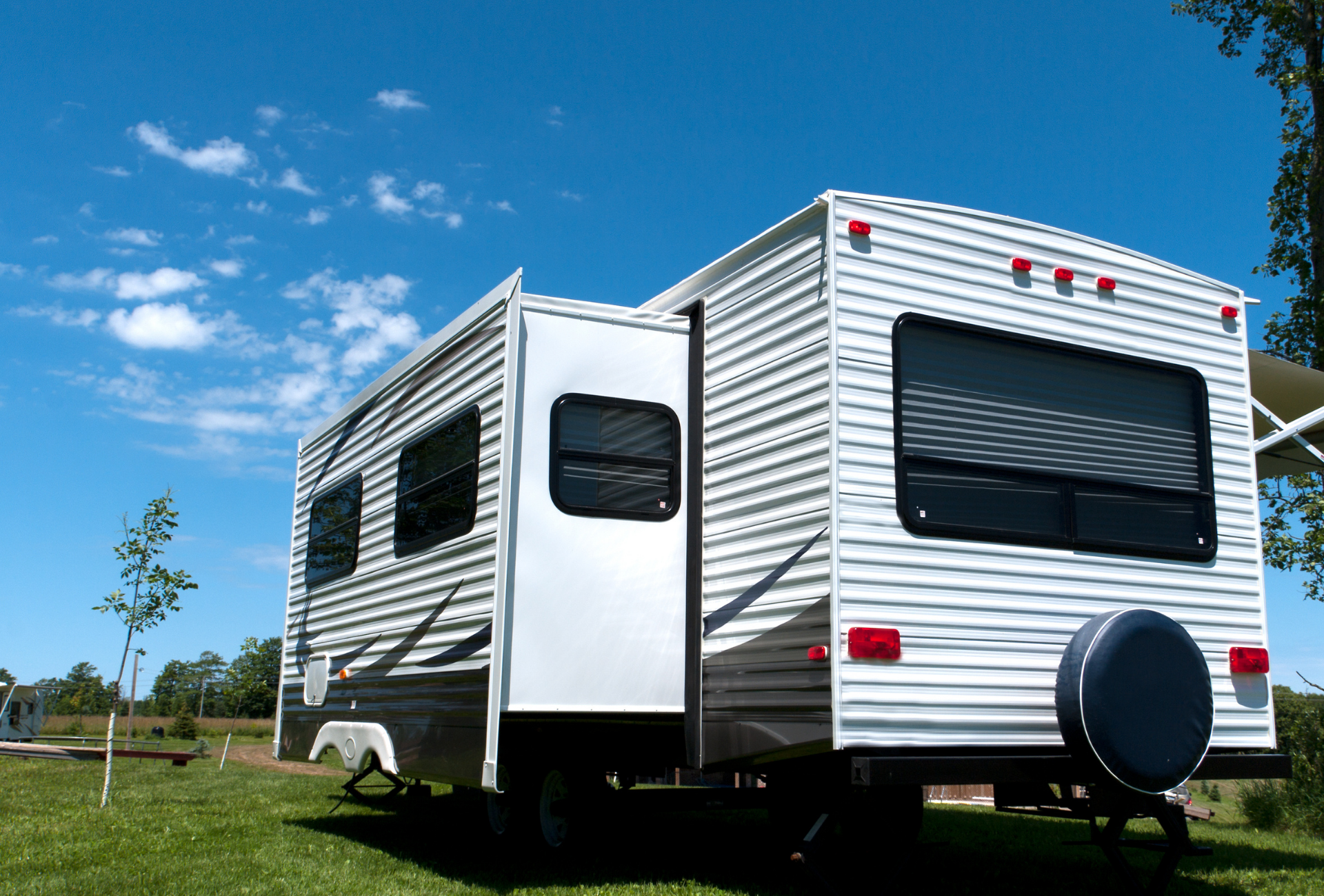 RV trailer parked on green grass under a blue sky.