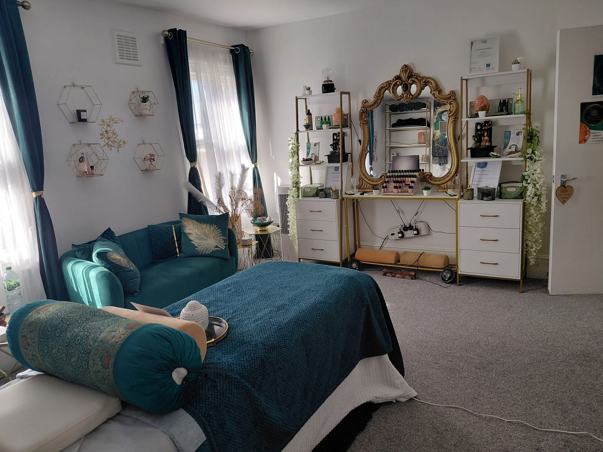 Teal chaise in a bright bedroom with ornate gold mirror, plants, and white dresser