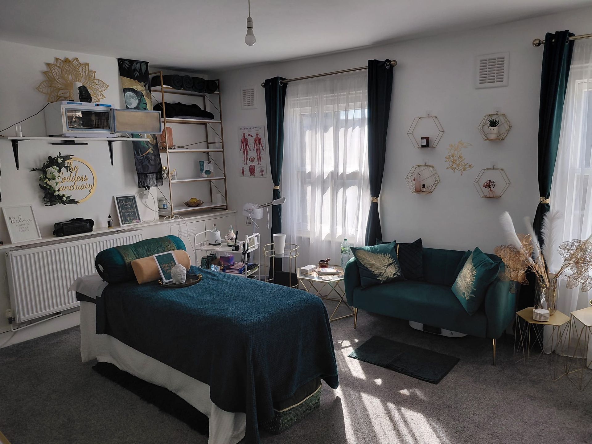 Cozy bedroom with a blue bedspread, teal sofa, white shelves, and floral wall decor by a window