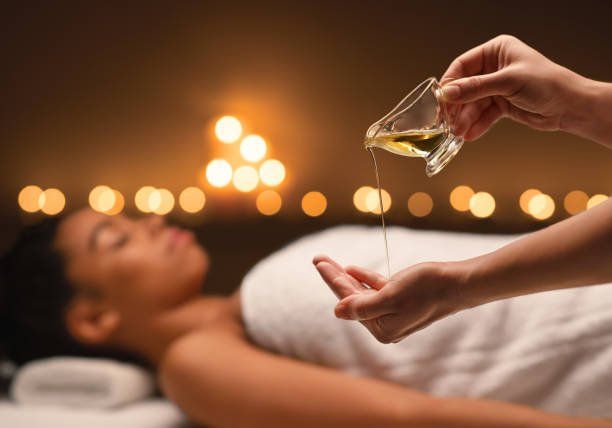 Spa therapist pouring oil over a client during a massage, with warm candlelight in the background