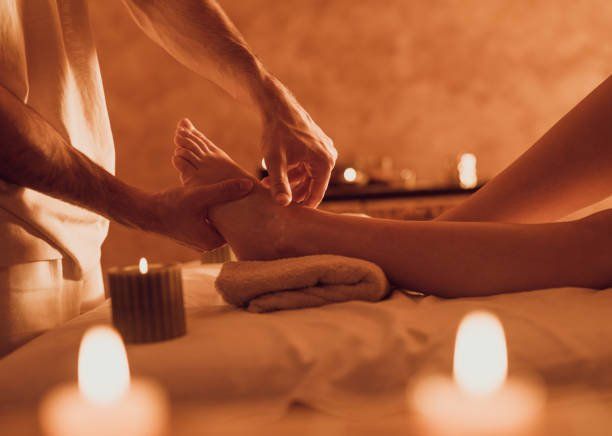 Massage therapist massaging a client’s foot on a massage table on top of a beige towel