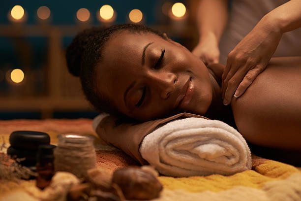 Person receiving a shoulder massage on a spa table, with towels and candles in warm light